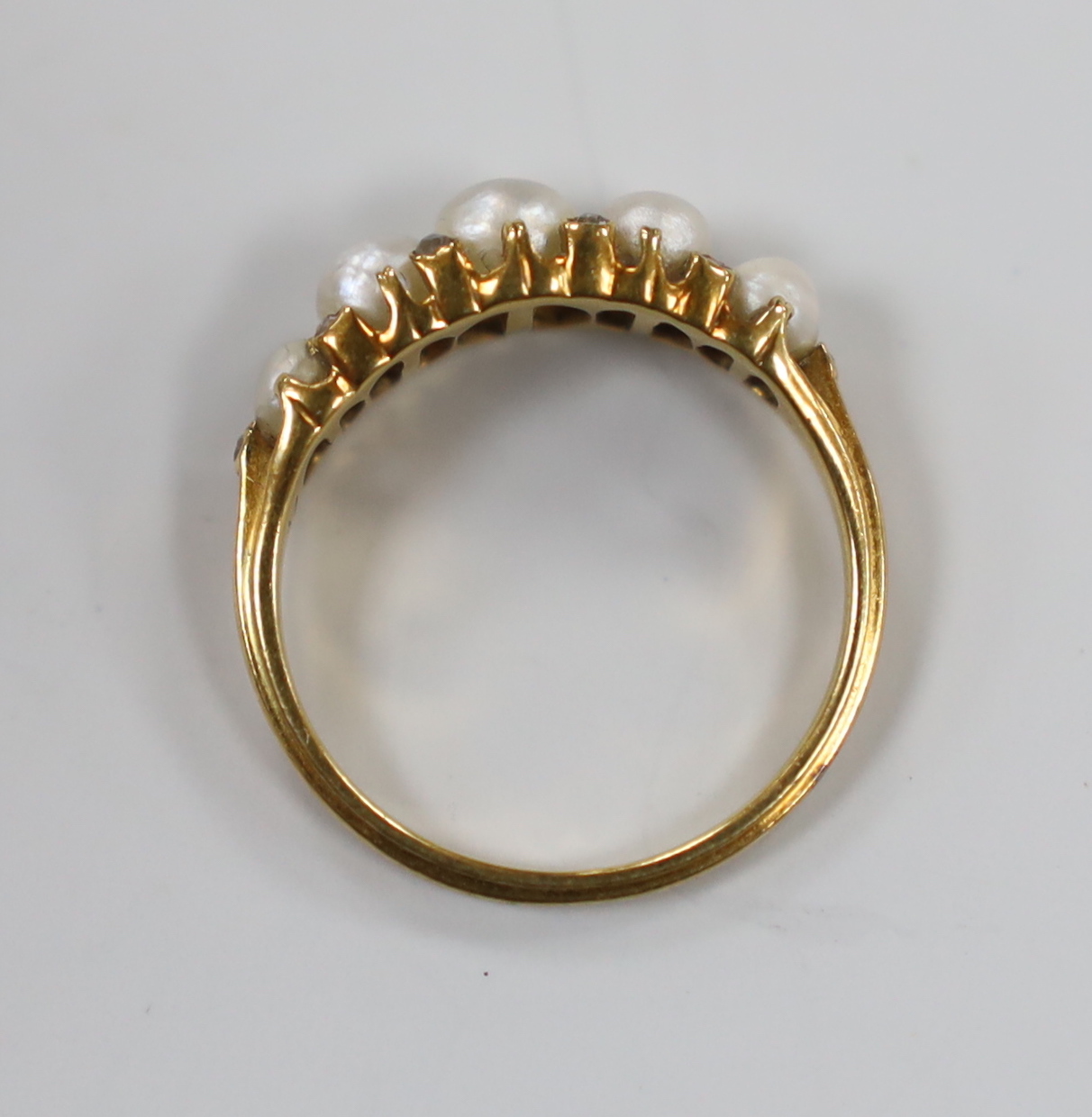 An Edwardian yellow metal and graduated split pearl set half hoop ring, with diamond chip spacers, size M, gross weight 3.1 grams.